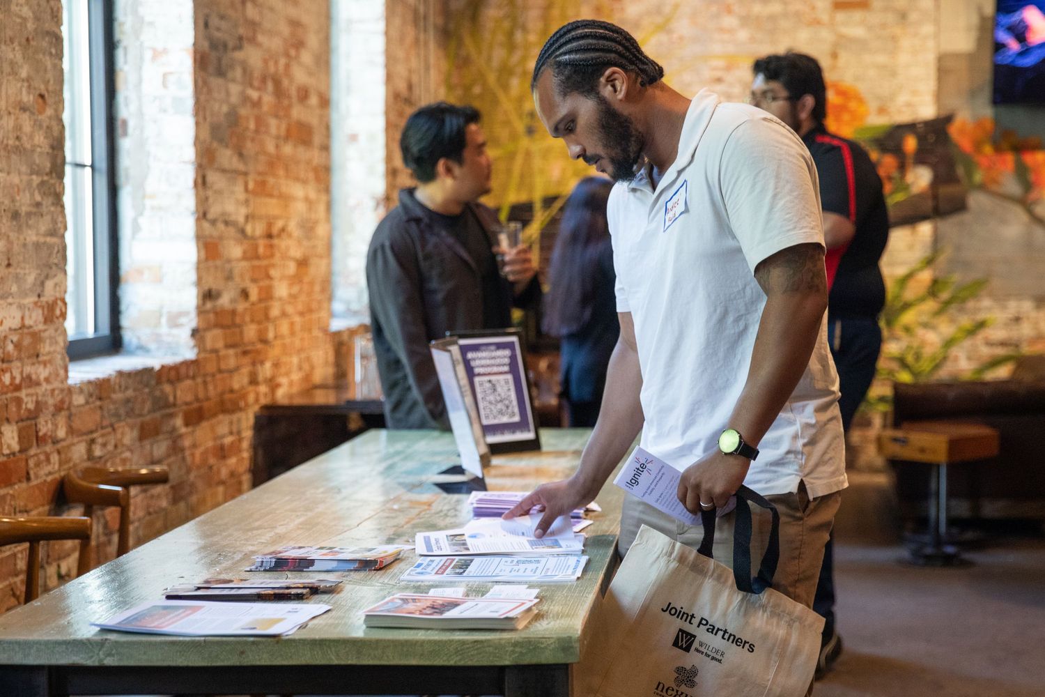 Visitor browsing through brochures and pamphlets at an information table inside a rustic brick-walled venue.