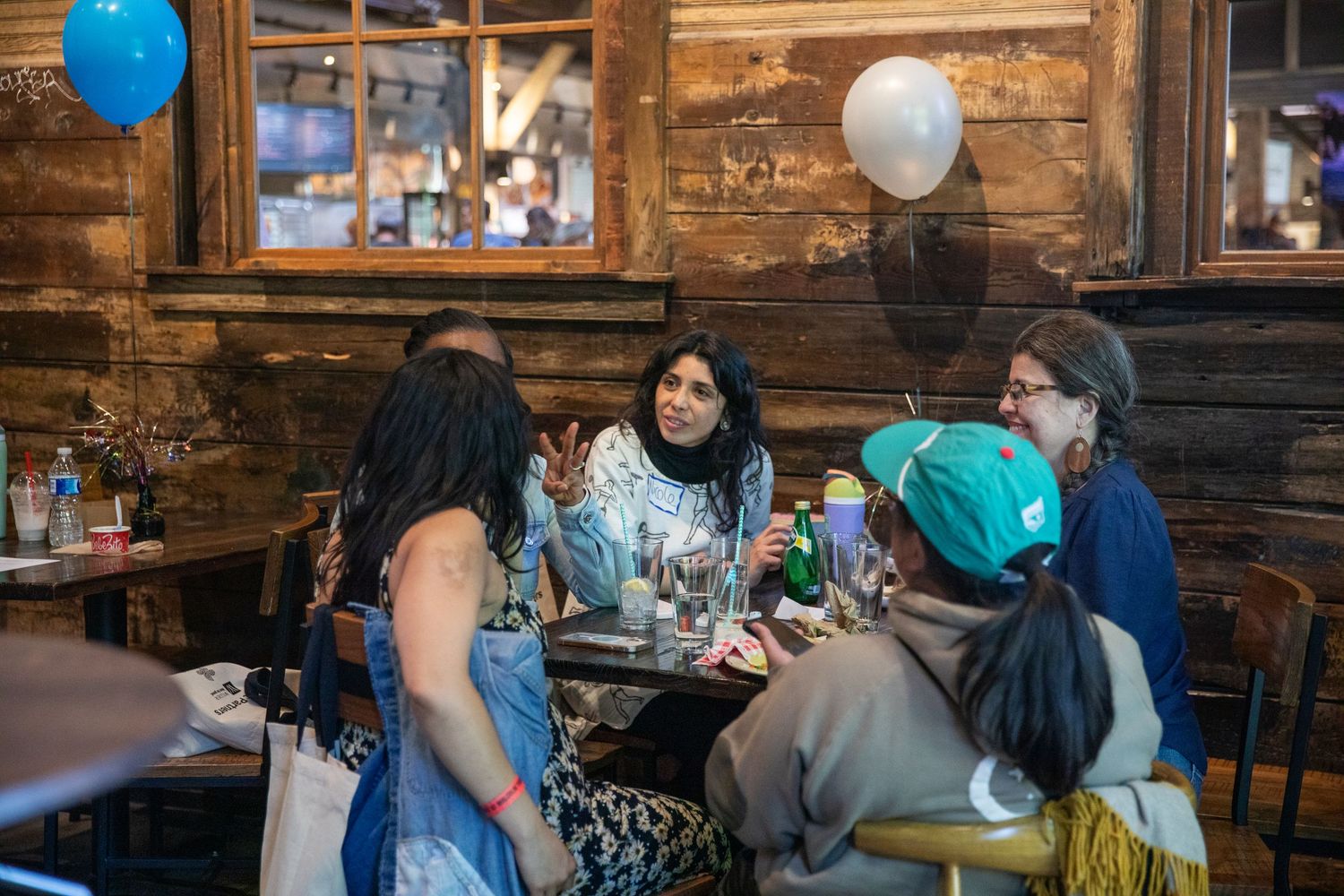 Friends gather for drinks at a rustic wooden bar restaurant with balloons in a casual, cozy atmosphere.