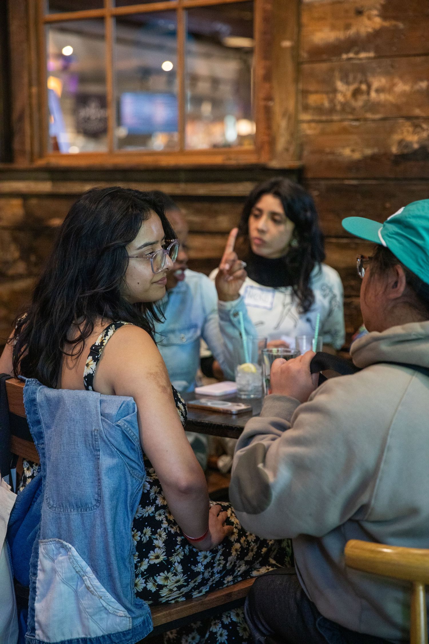 A group of friends having a conversation at a rustic restaurant with wooden walls and ambient lighting.