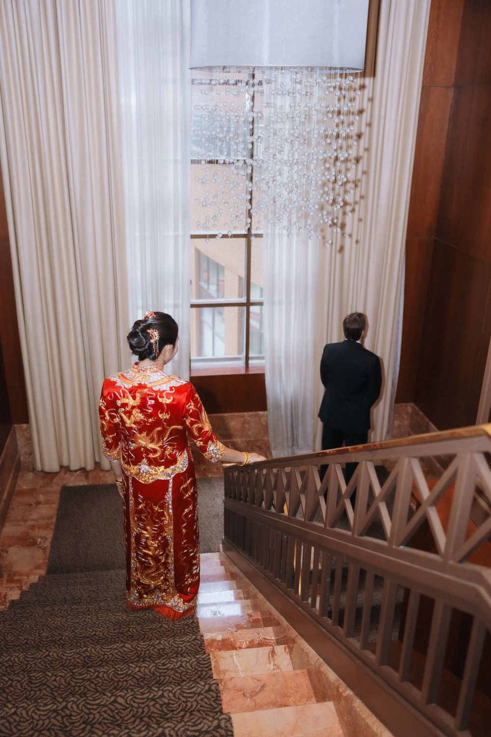 A couple stands in a hallway with sheer curtains and wooden railings during a wedding first look.