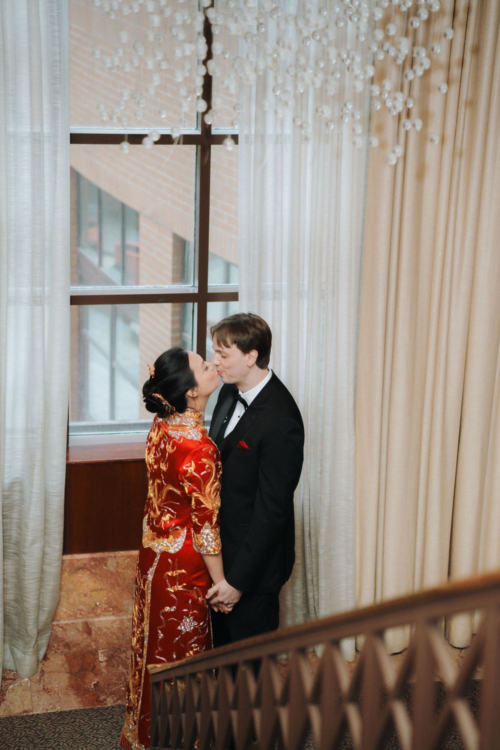 A wedding couple shares an intimate moment in an elegant venue with sheer curtains and chandeliers.