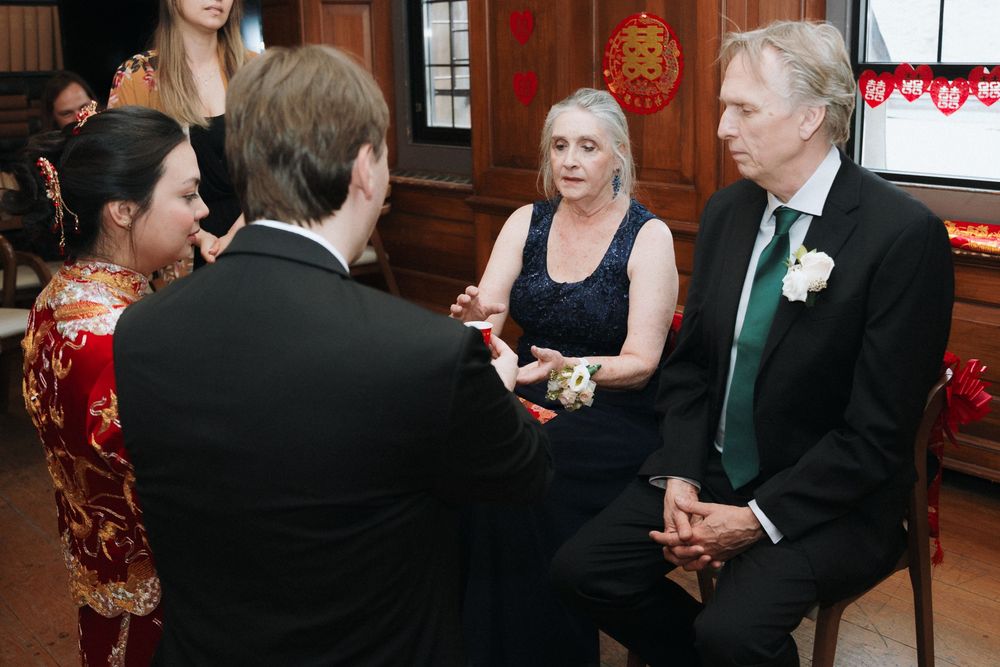 Wedding guests in formal attire having an intimate conversation at a reception with traditional Chinese decor.