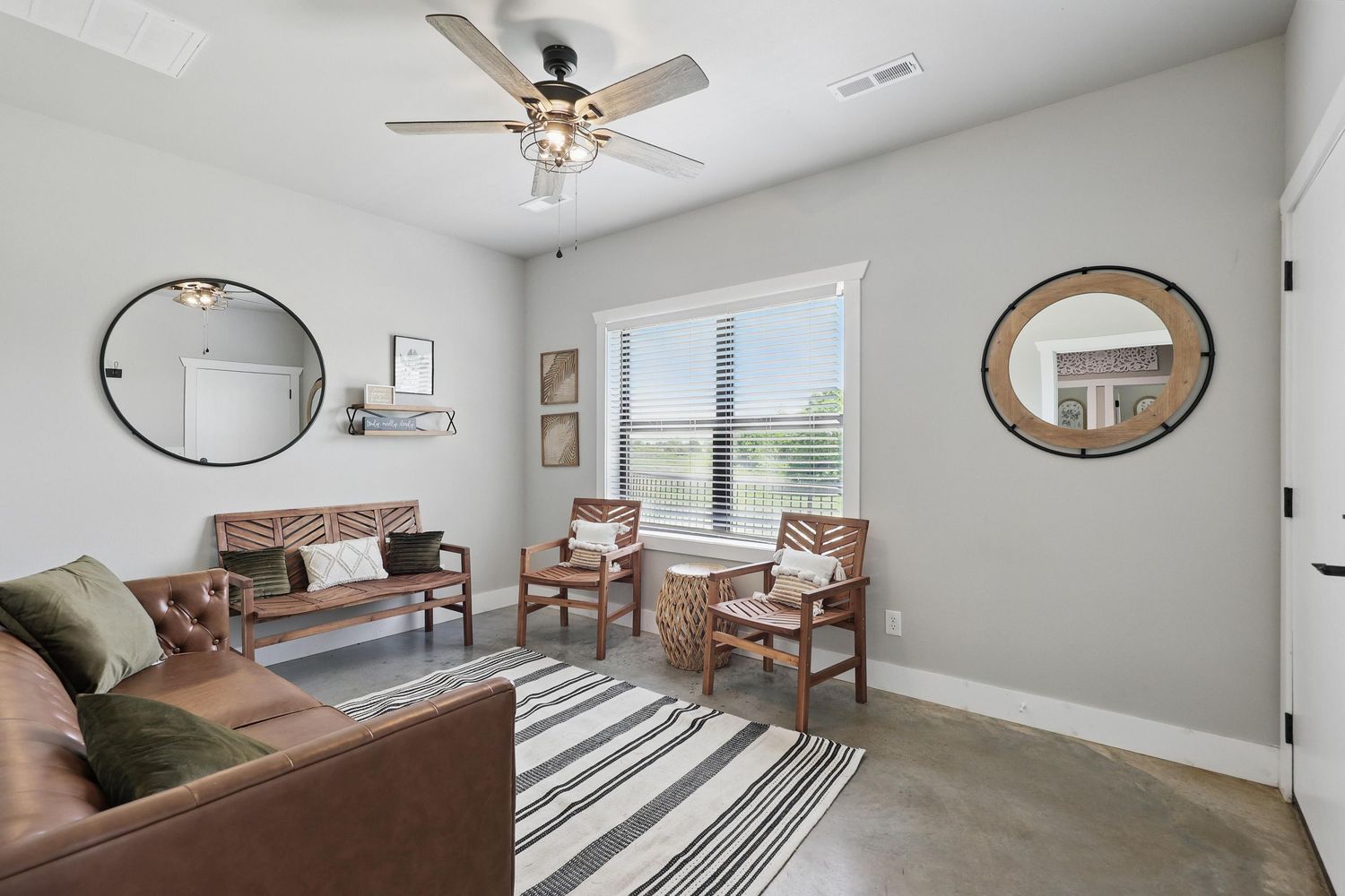 Modern living room featuring brown leather sofa, striped area rug, round mirror and minimalist wall decor.