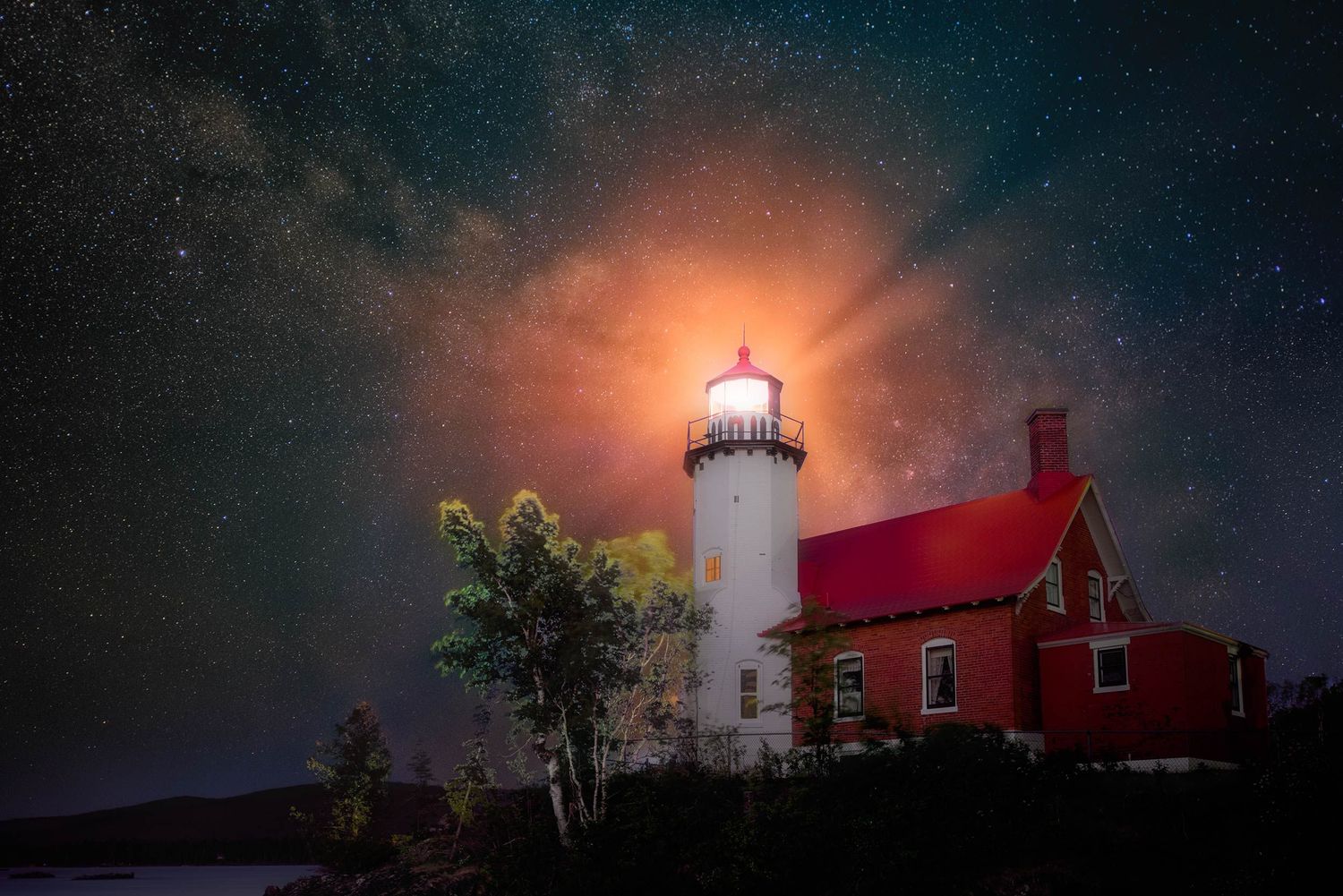Lighthouse with red-roofed building illuminated at night under starry sky with dramatic moonlight glowing through clouds.