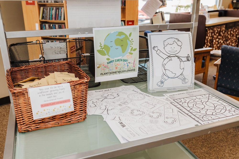 A collection of children's learning materials including coloring pages and a woven basket full of wildflower seeds on a table.