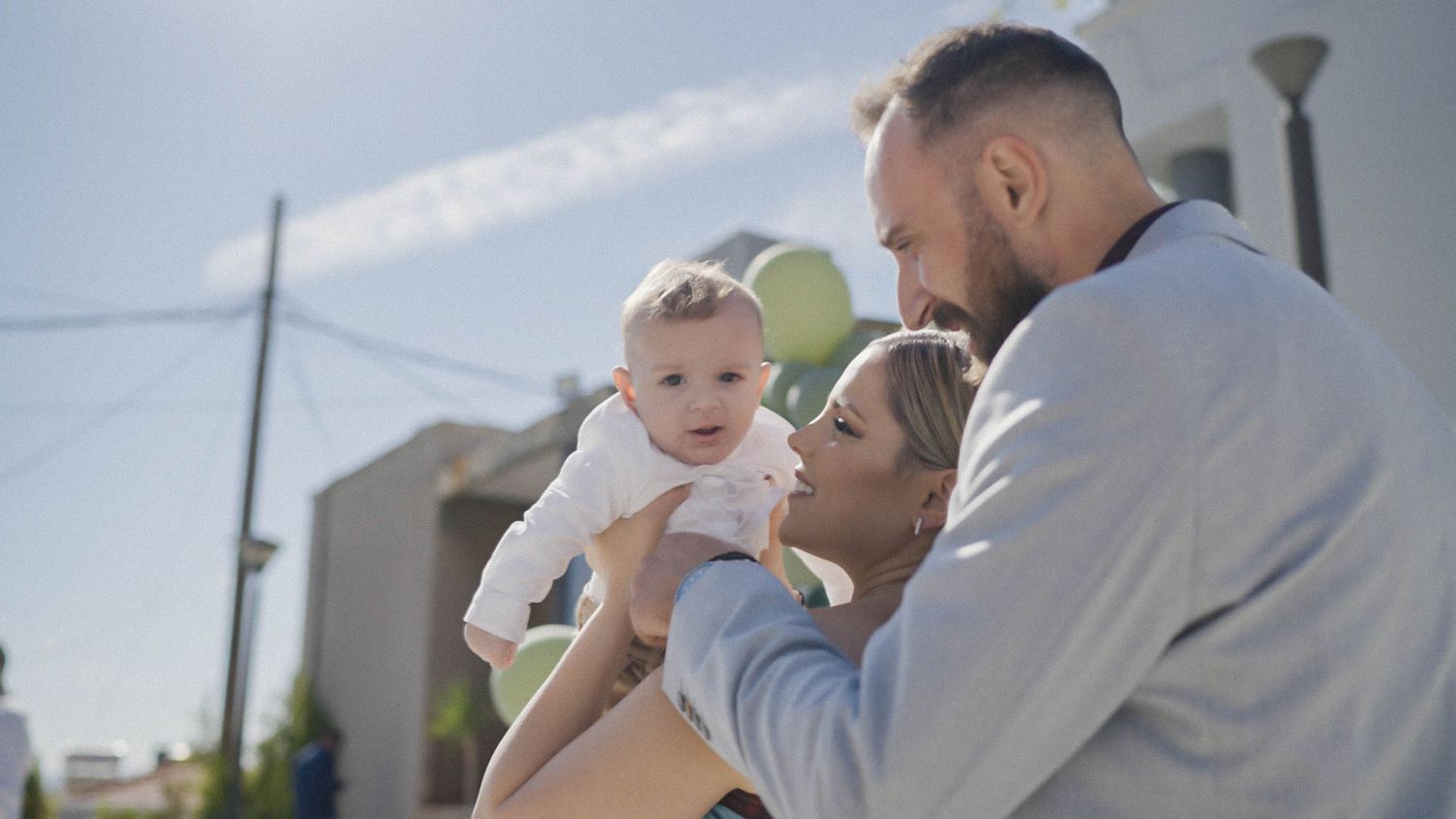 A happy family enjoying a tender moment together outdoors on a sunny day near a building.