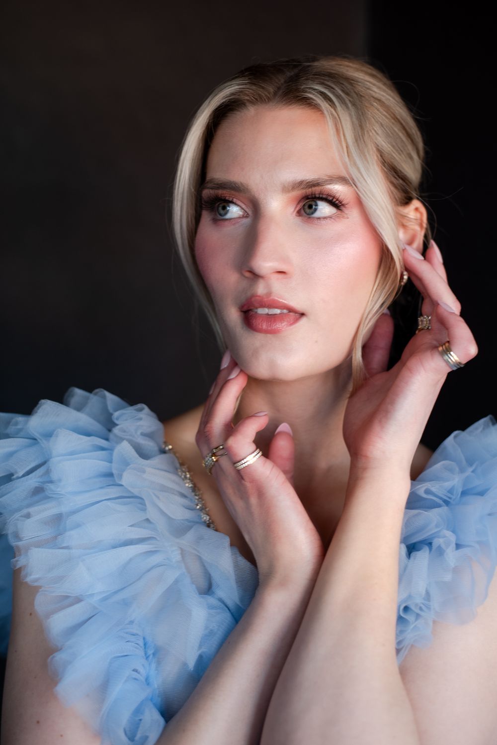 A person wearing a light blue ruffled tulle dress poses against a dark background in a glamorous portrait.