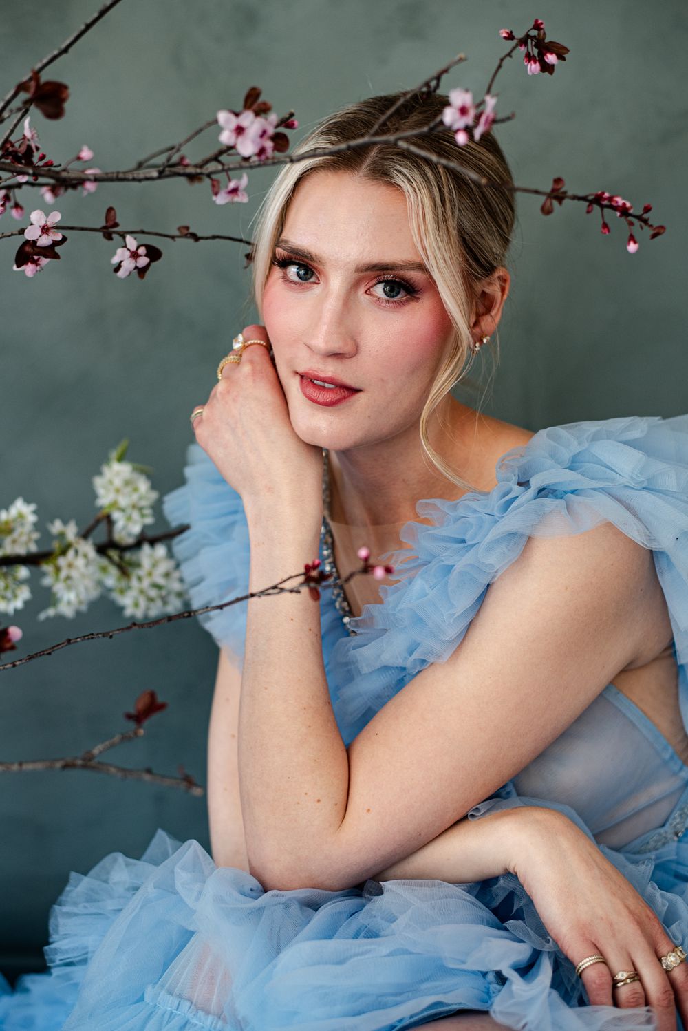 A romantic portrait with cherry blossoms featuring a light blue tulle gown against a moody gray backdrop.