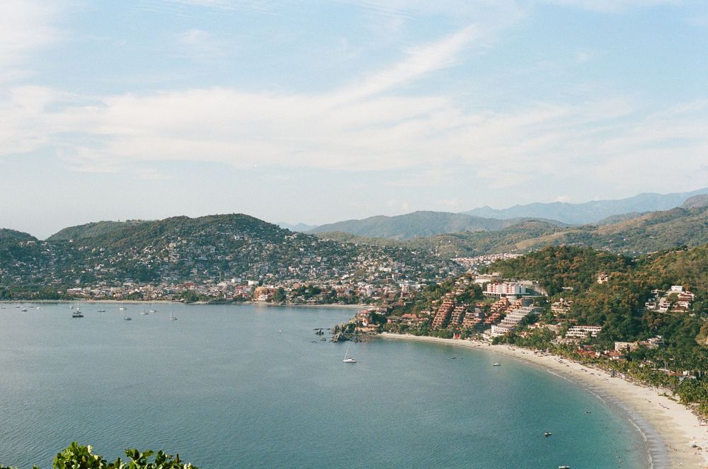 Aerial view of a coastal town with curved beach and mountains in the background.