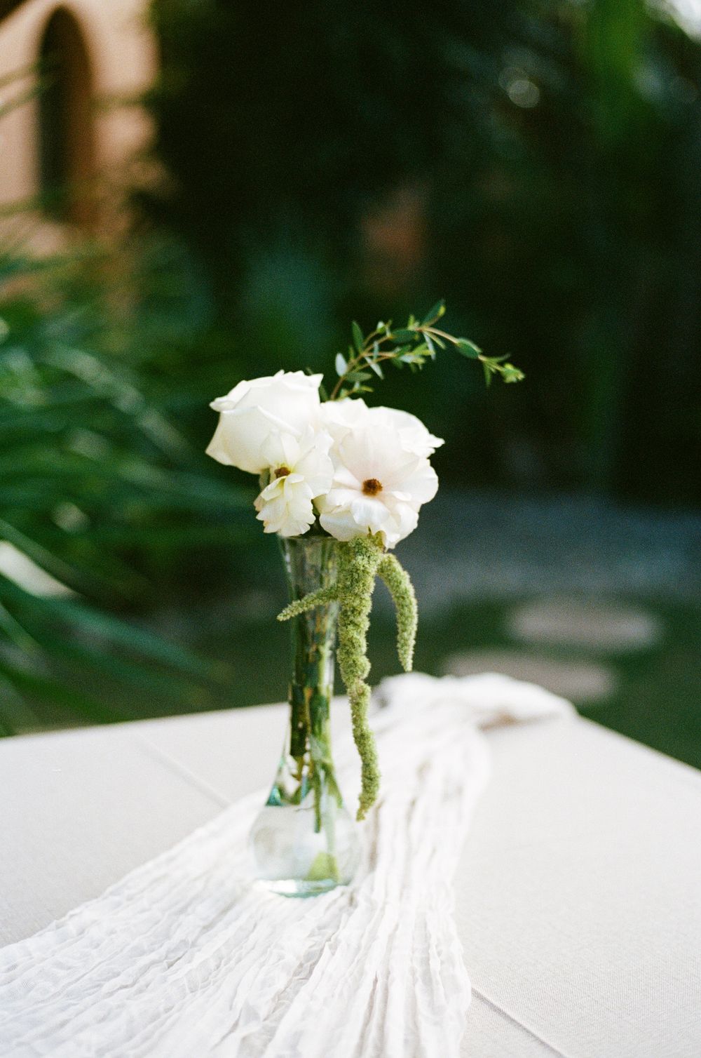 Simple white flowers arranged in a clear glass vase on a white tablecloth.