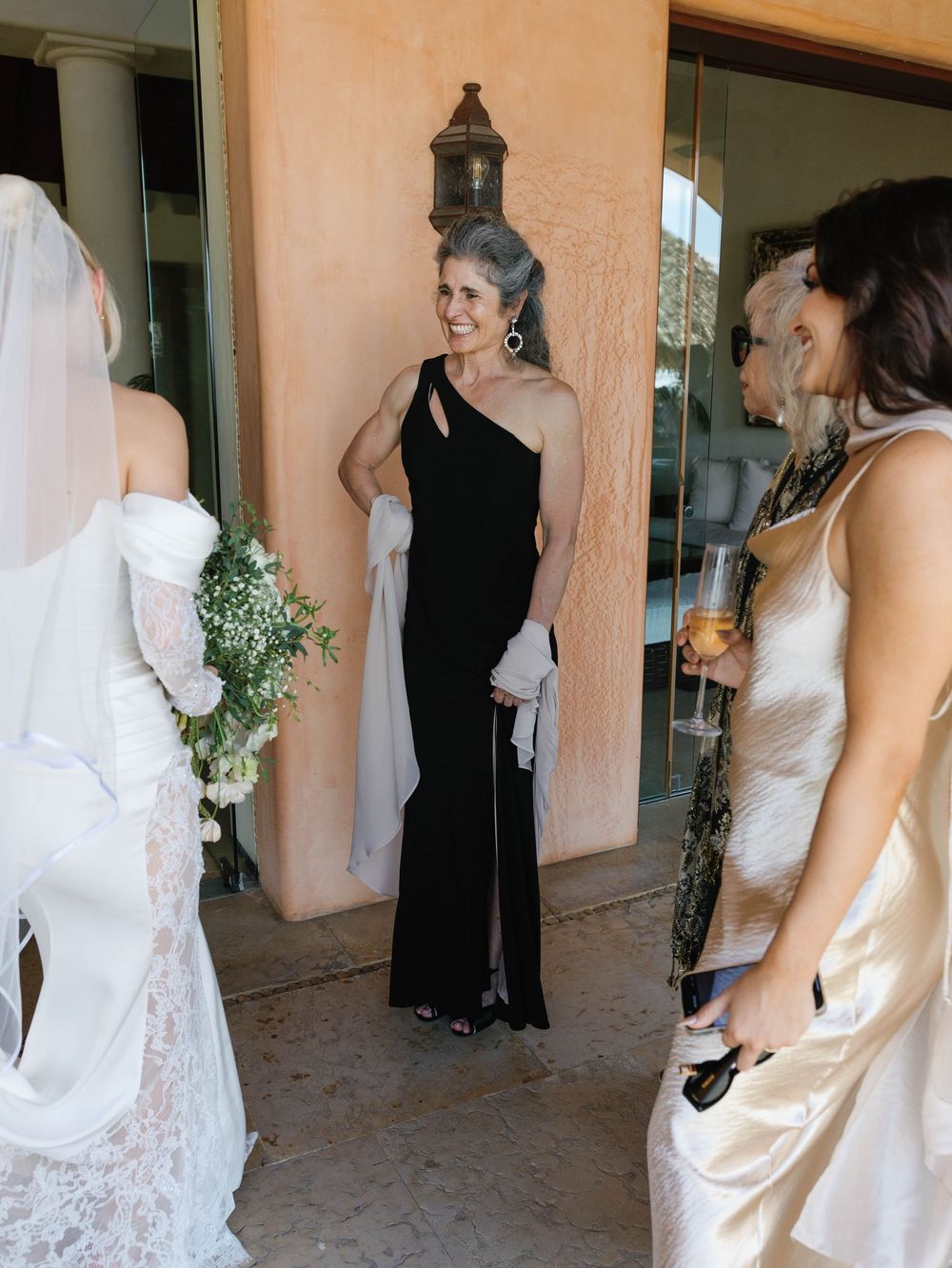 Wedding party members in elegant dresses gather for conversation on a terrace.