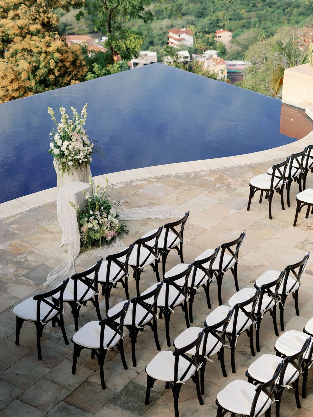 Elegant outdoor wedding ceremony setup with black chairs and white floral arrangements.