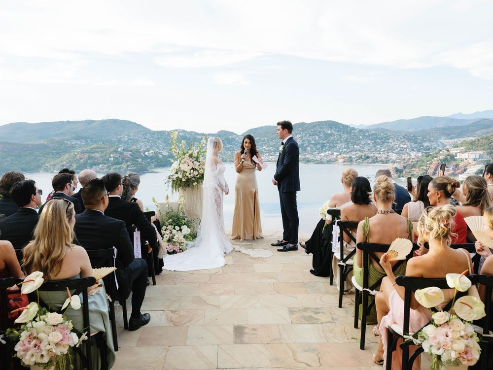 Outdoor wedding ceremony on a stone terrace overlooking a scenic mountain lake backdrop with floral arrangements.