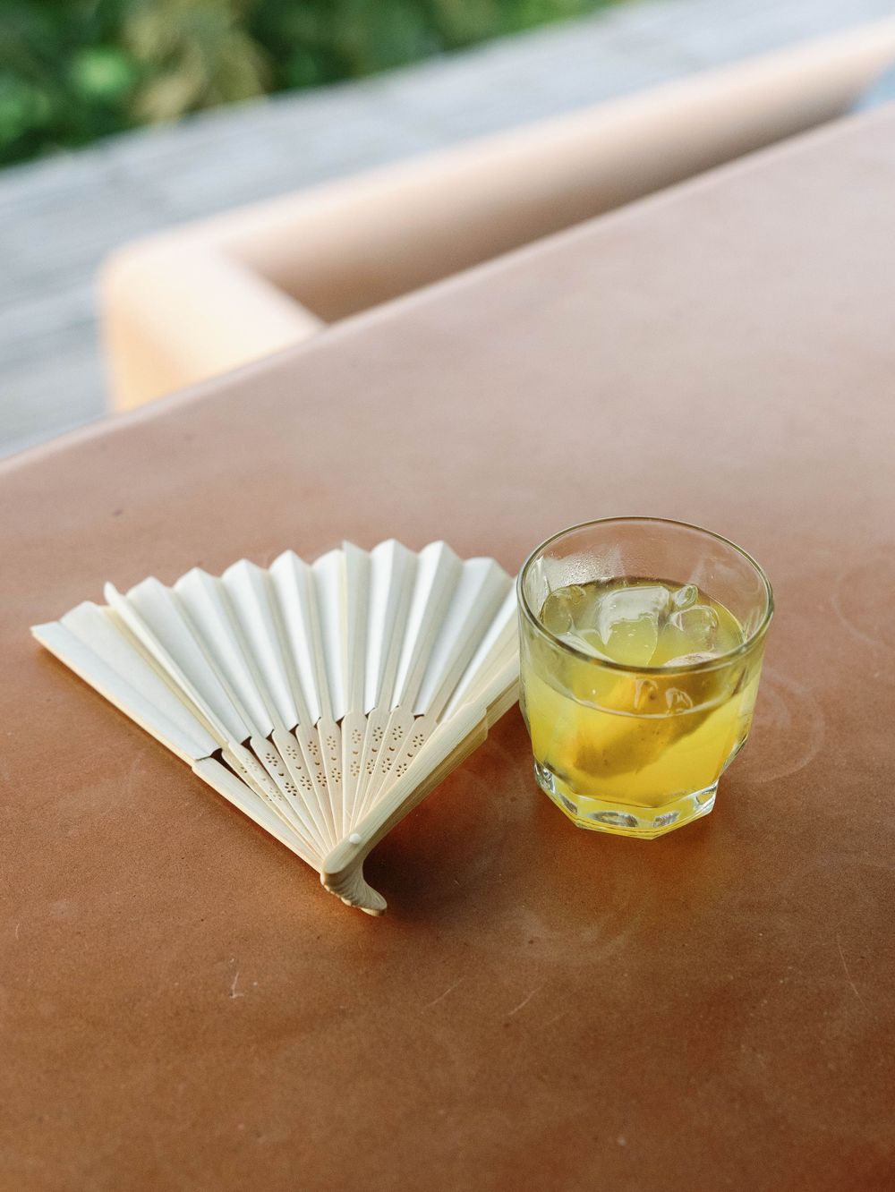 White paper fan and glass of whiskey on rocks on wooden table at wedding reception.