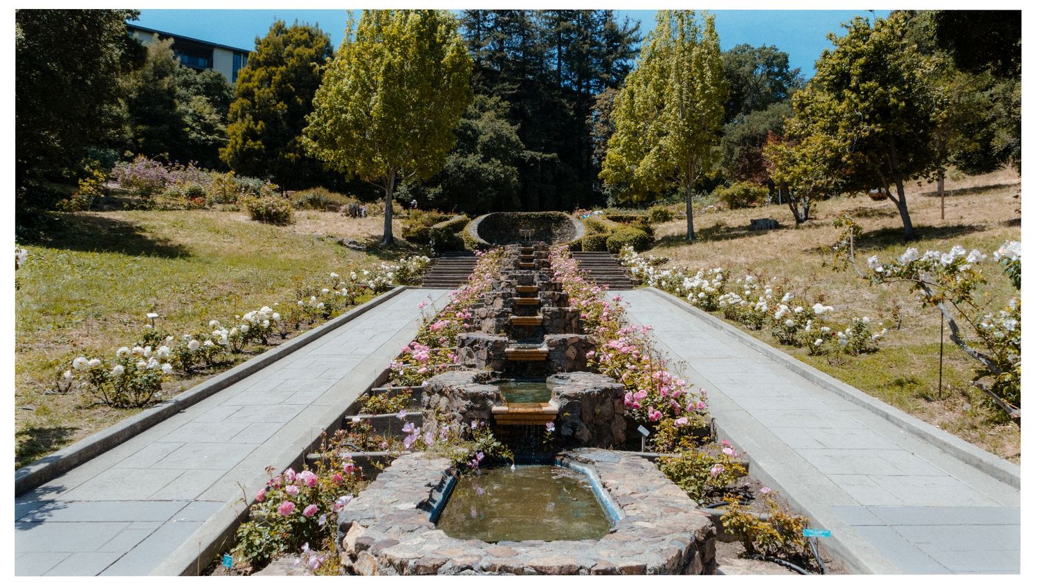 A symmetrical garden path with cascading fountains and stone features leads through trees and landscaped grounds.
