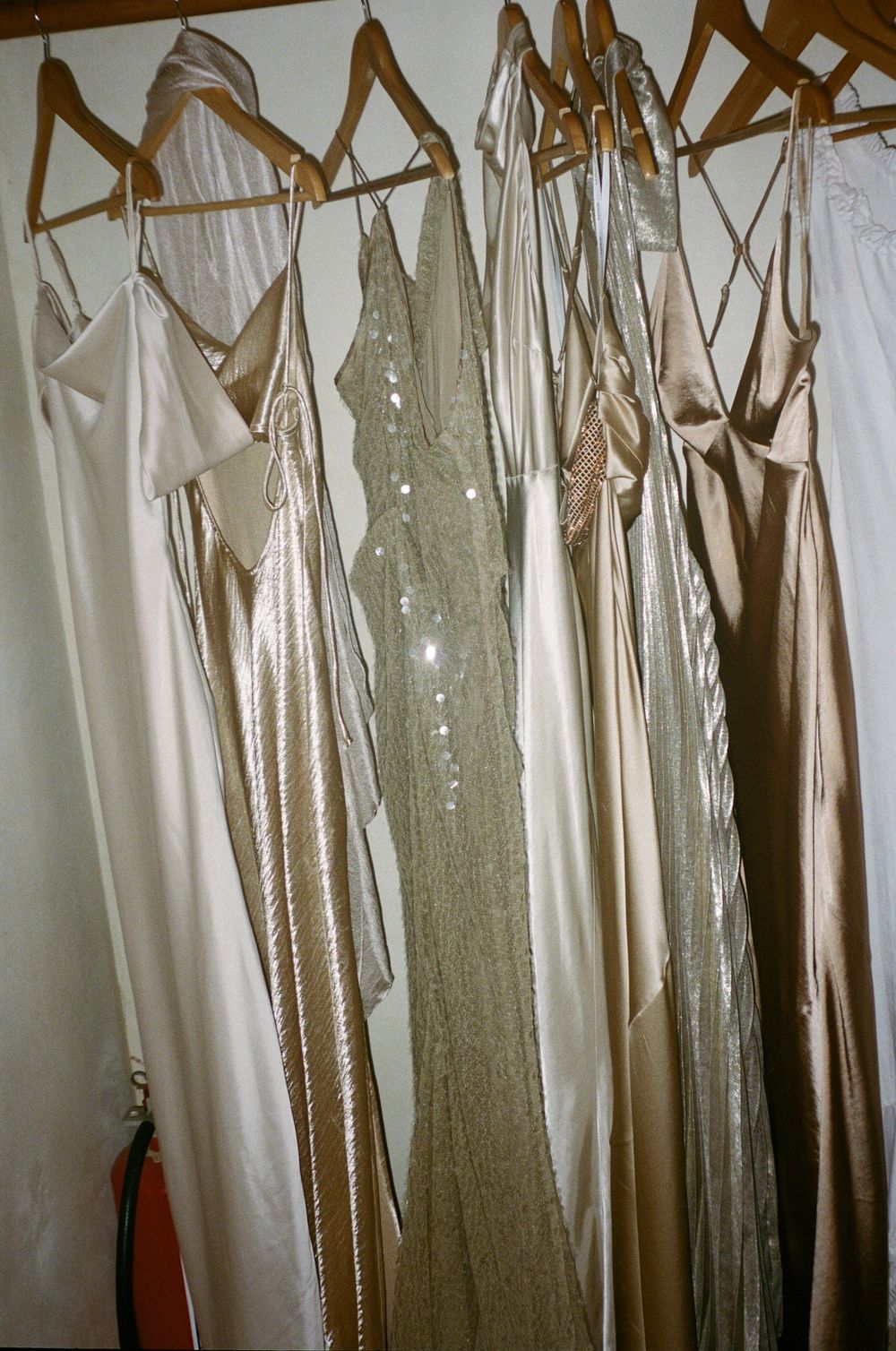 Row of elegant champagne and ivory bridesmaid dresses hanging on wooden hangers.
