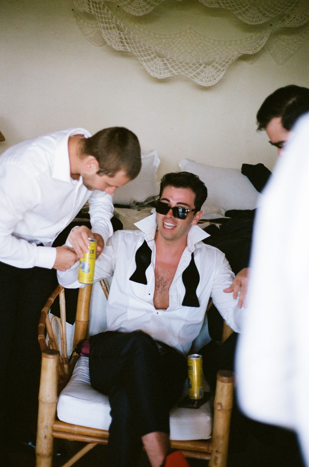 Casual gathering in white attire with beverages and laughter on bamboo chairs.
