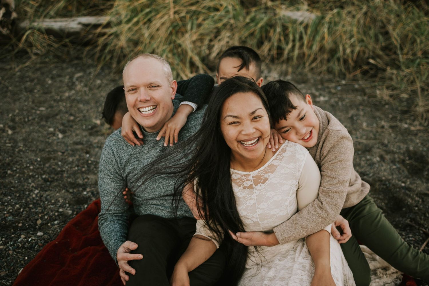 Beautiful portrait photography of family sitting on Madrona Point beach grass on Vancouver Island during golden hour and laughing