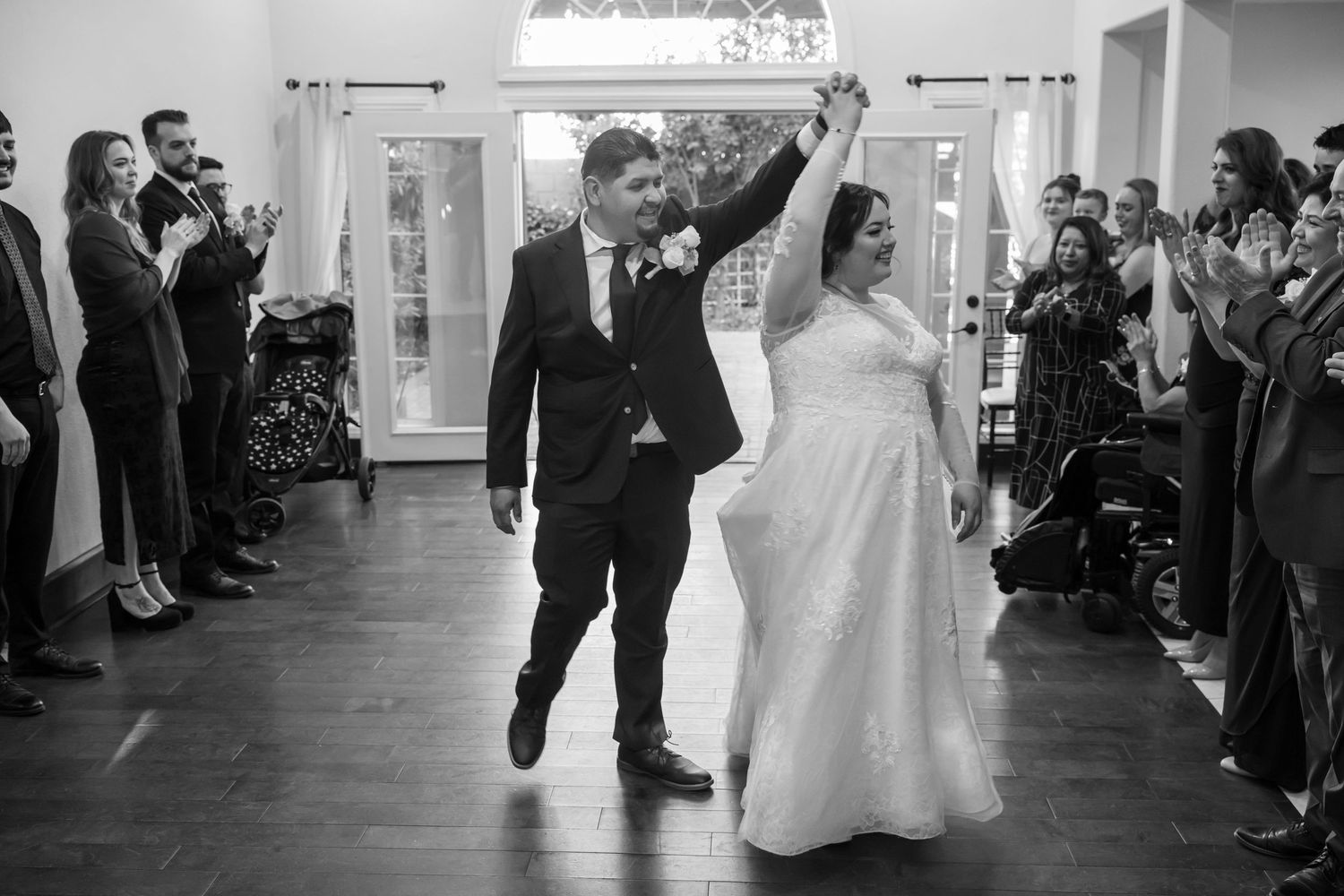 Black and White Photo of a newly married couple doing an entrance to a reception with everyone clapping.
