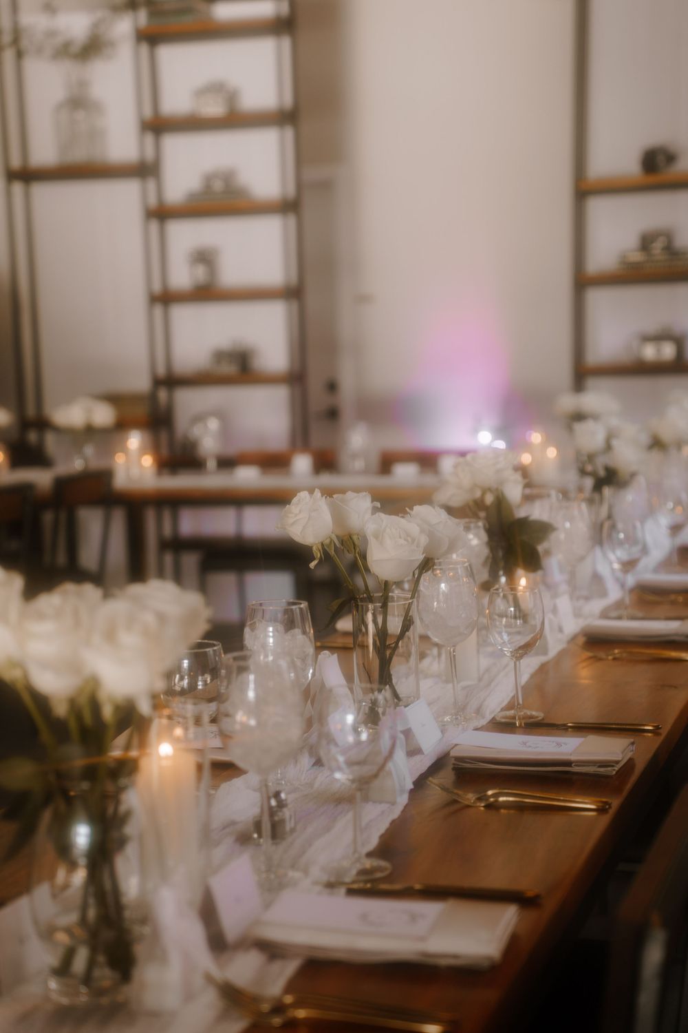 Close-up of an elegant table setting with white roses in vases, glassware, and candlelight.