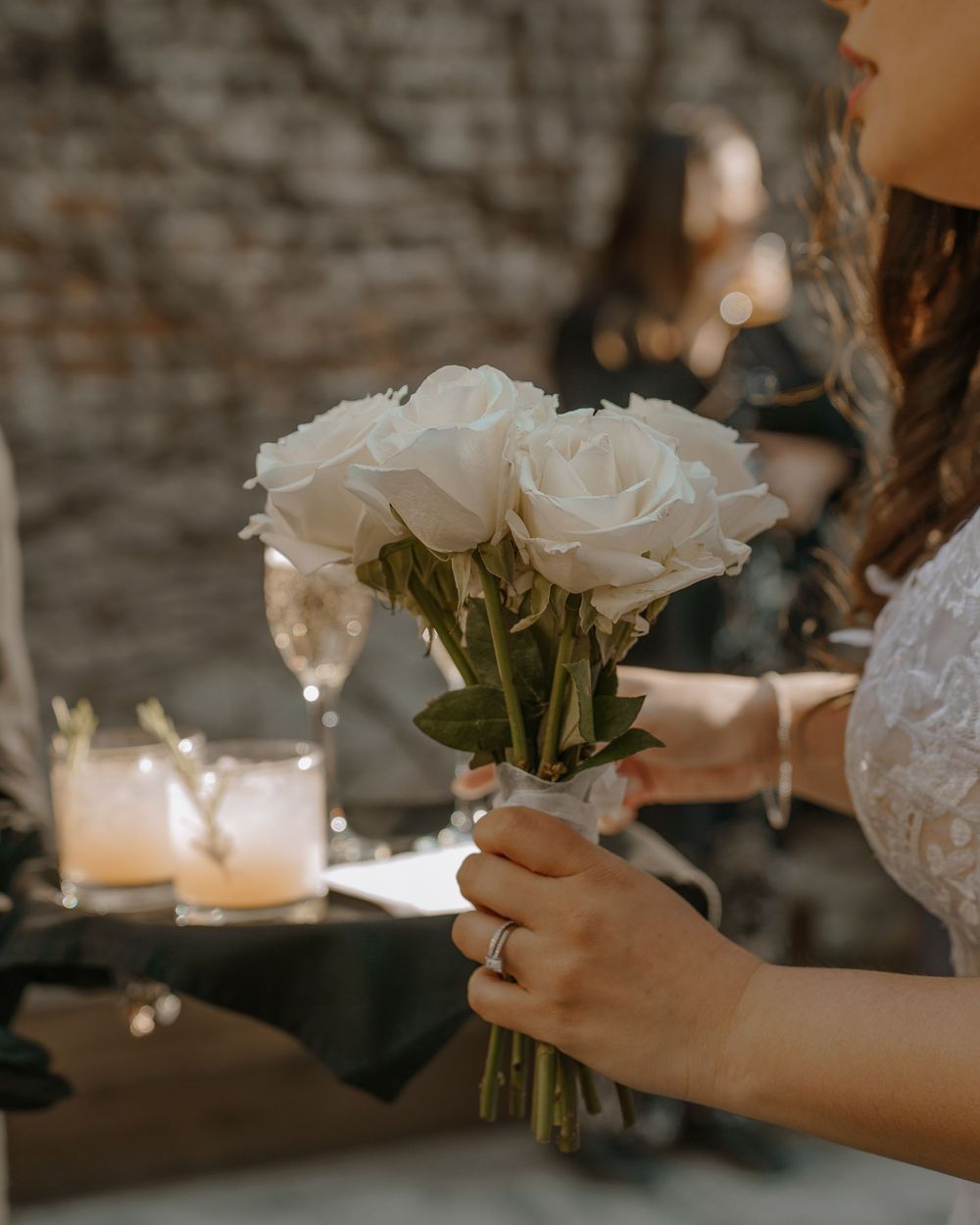 A person holding a bouquet of white roses with lit candles in the background creating a romantic ambiance.