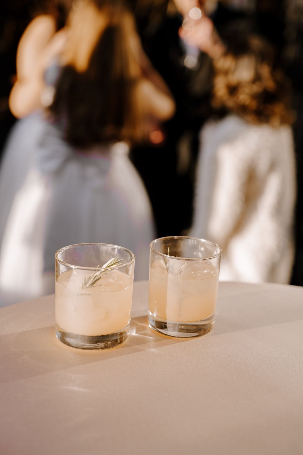 Two frosted glass cocktails with rosemary garnish on a white surface at an event.