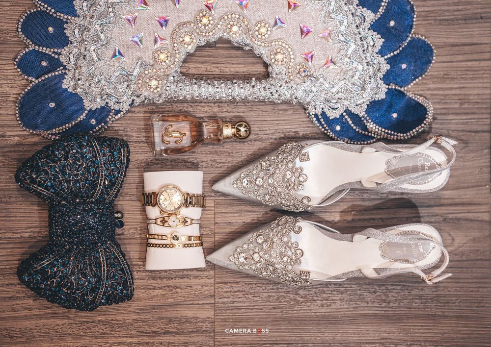Wedding accessories including sparkly silver shoes, a navy blue bow, pearl bracelets and floral headpiece on wooden surface.