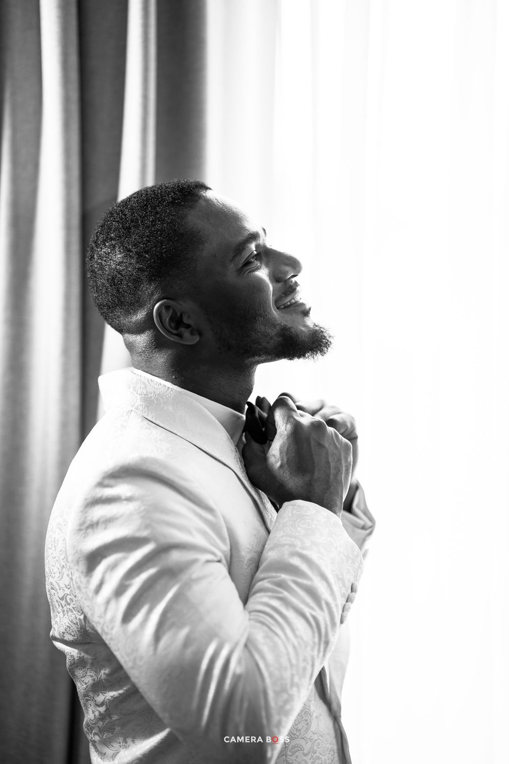 A person wearing a white suit jacket and tie adjusts their collar while looking upward in contemplative black and white portrait.