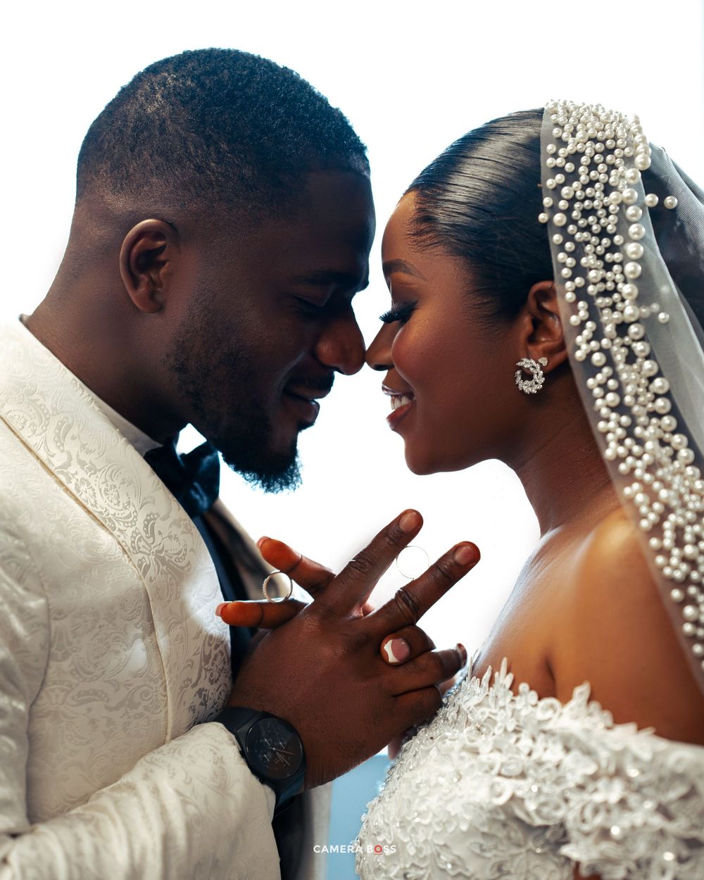 A tender newlywed couple in wedding attire share an intimate close moment while holding hands.