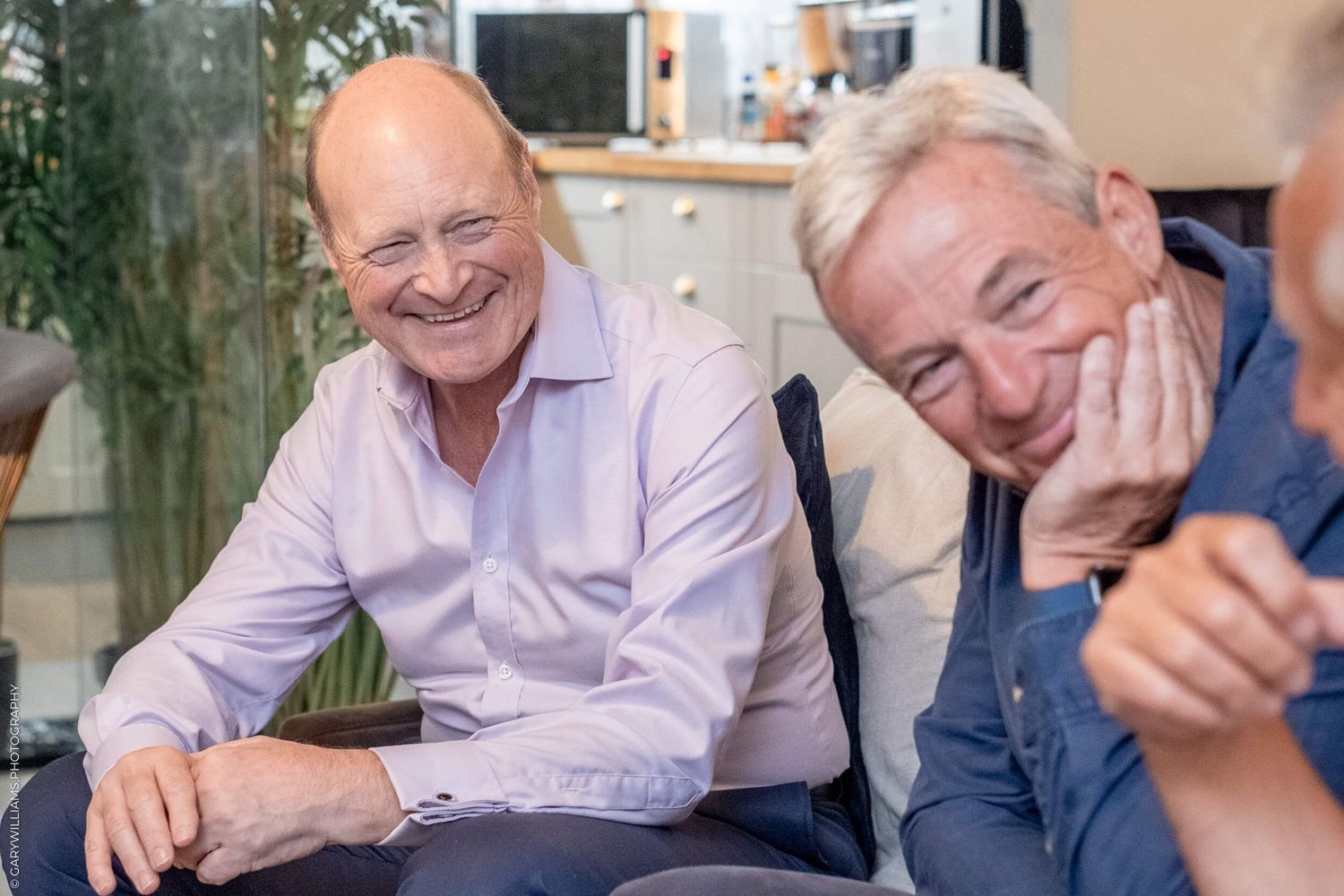 Two senior men laughing together while relaxing on couch.