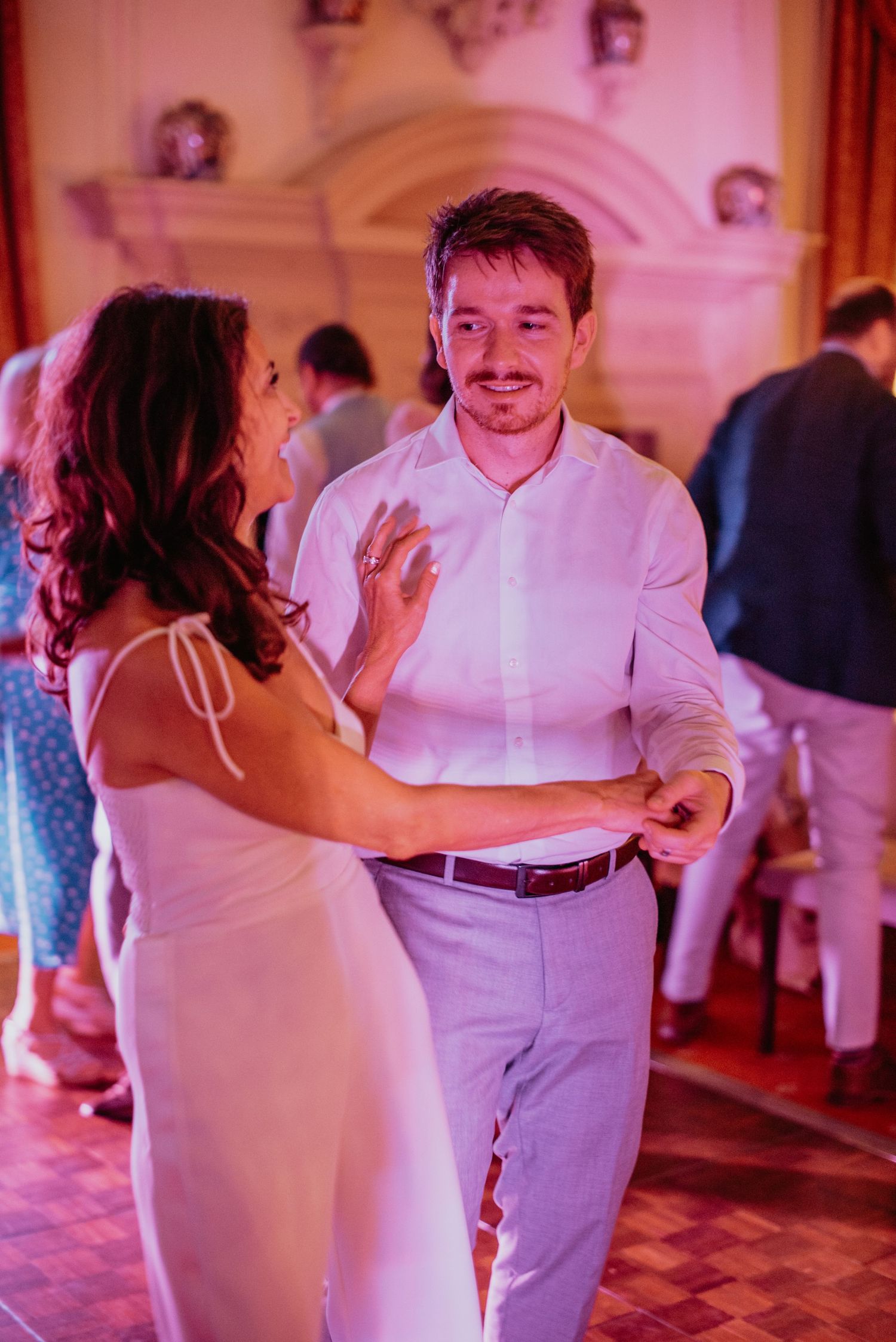 Dancing couple in pink-lit room share a romantic moment at what appears to be a wedding reception or formal event.