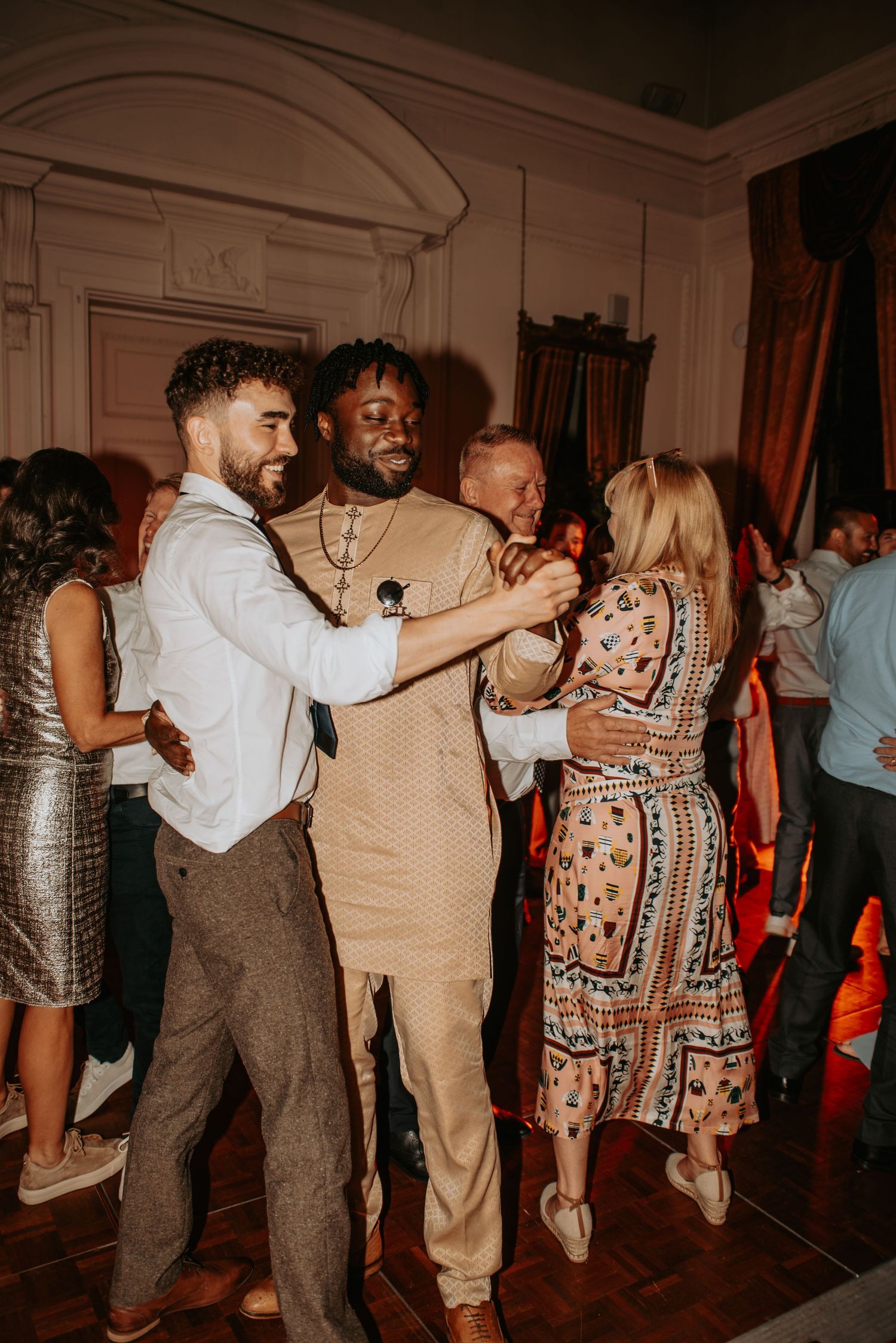 People dancing and enjoying themselves at an indoor party with warm lighting and elegant architectural details.