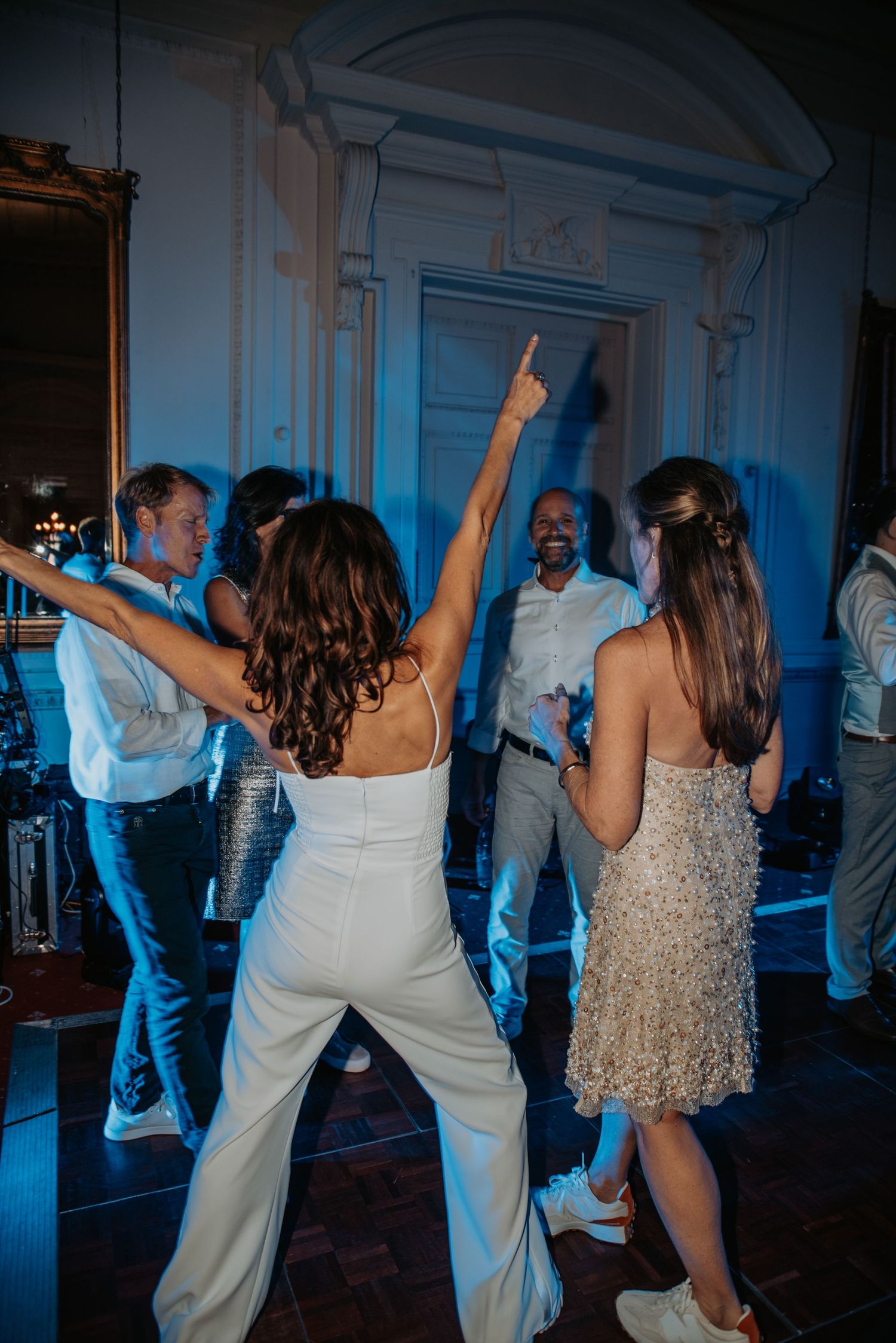 People dancing and celebrating at an elegant venue with blue lighting and ornate architectural details.