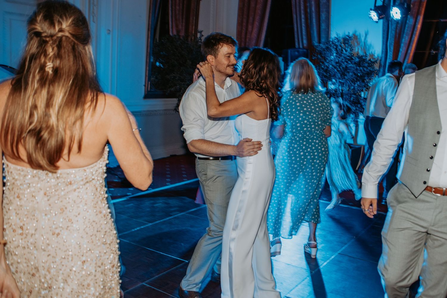Couple embraces while slow dancing on a blue-lit dance floor at an evening wedding reception.