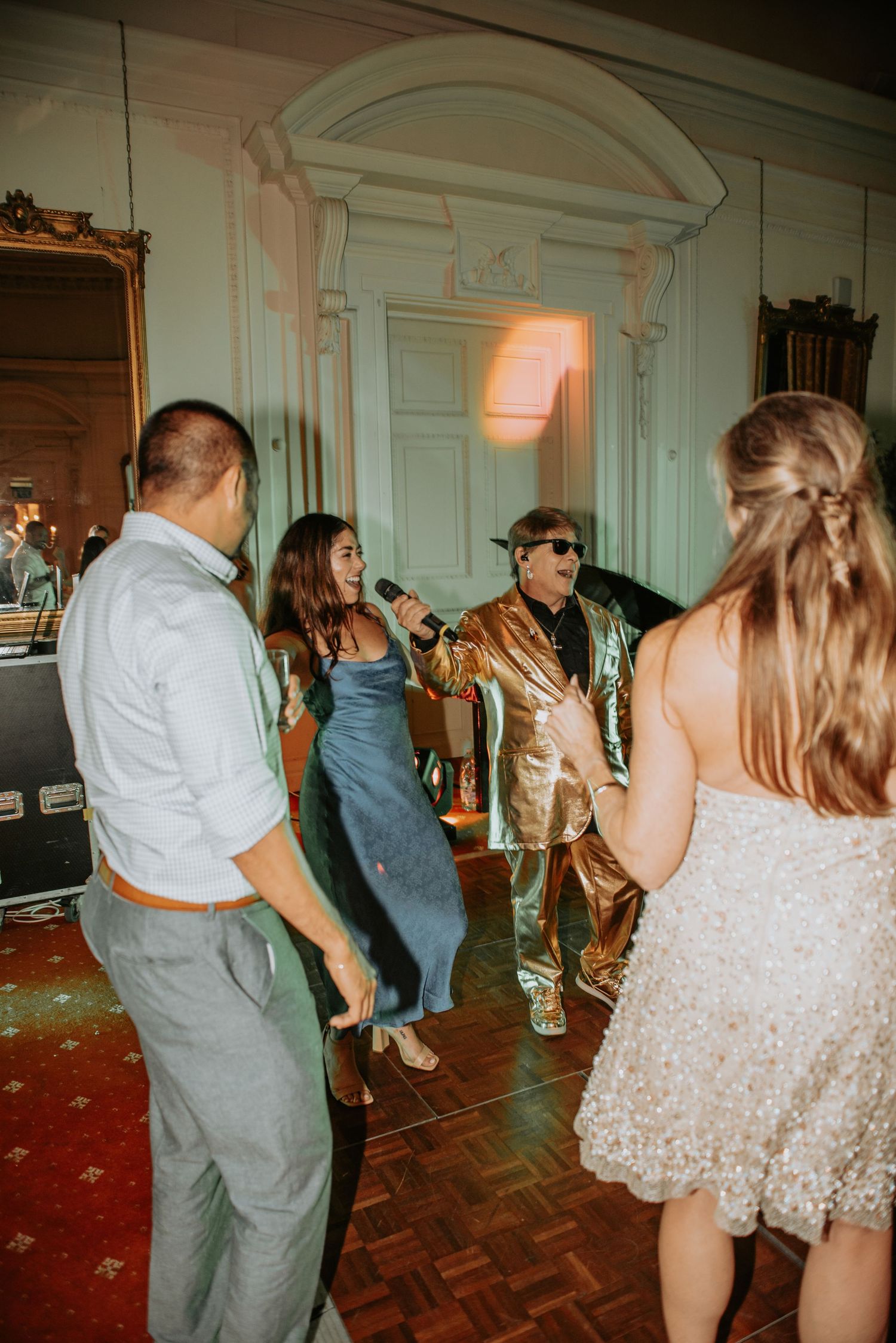Party guests dancing and enjoying themselves at an elegant venue with white walls and parquet flooring.