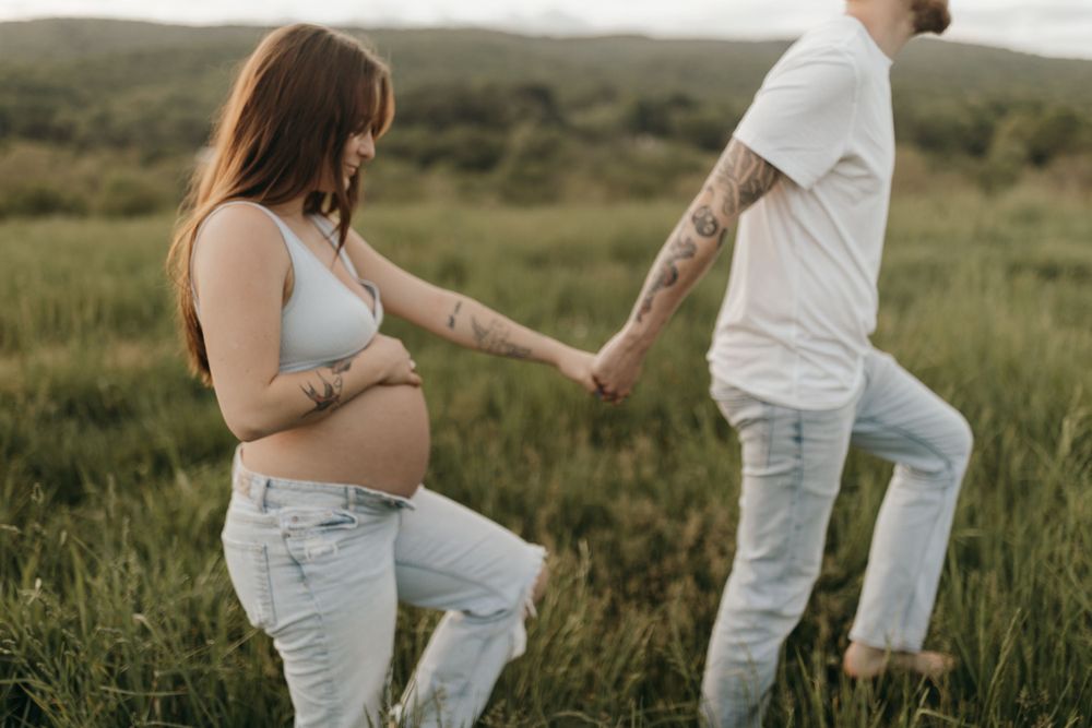 Expectant couple holding hands in a field during a casual maternity photoshoot at dusk.