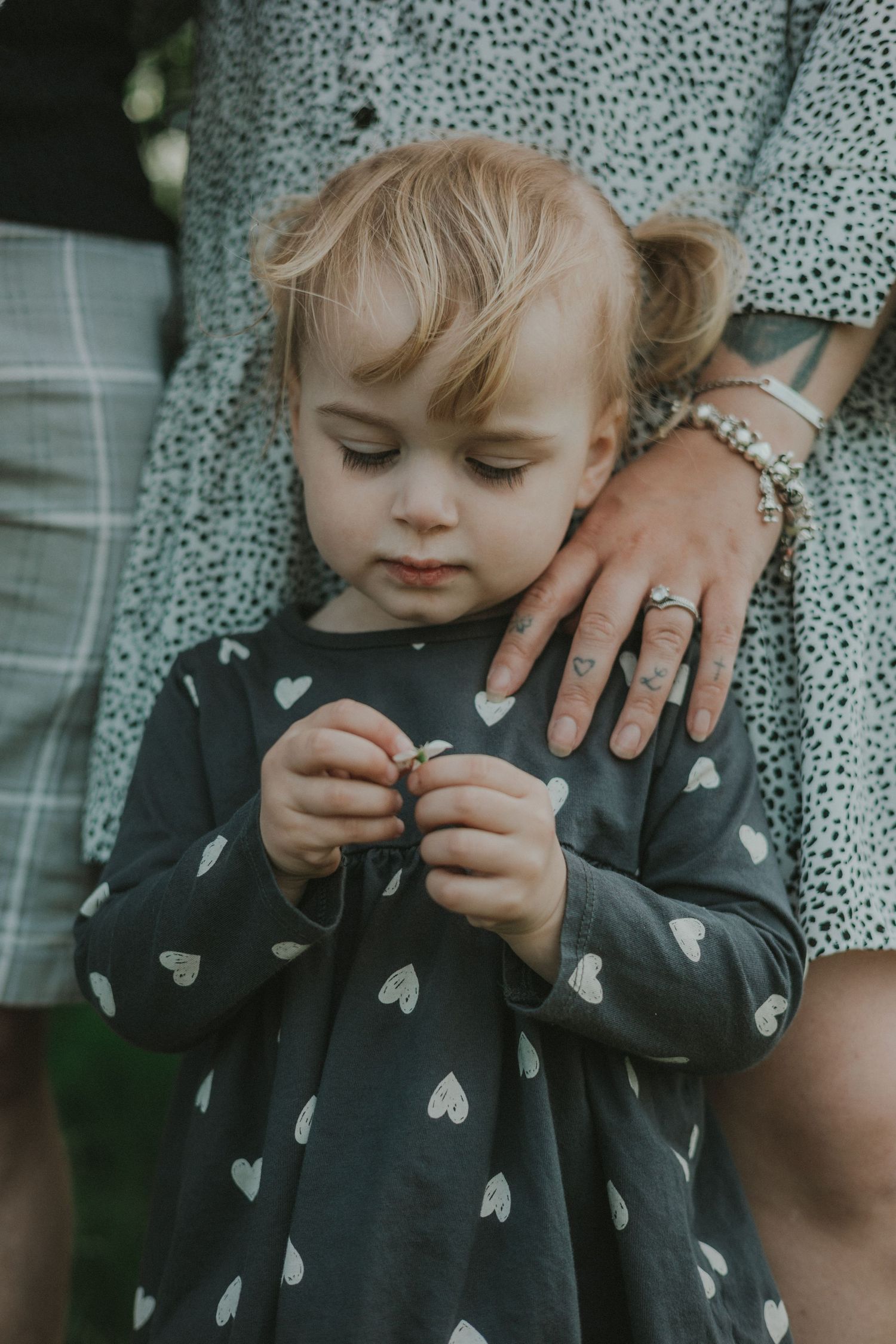 little girl looking at hands holding flower remains, mums hand on her shoulder,at family sessionNeedham Lake, Suffolk, in colour muted tones