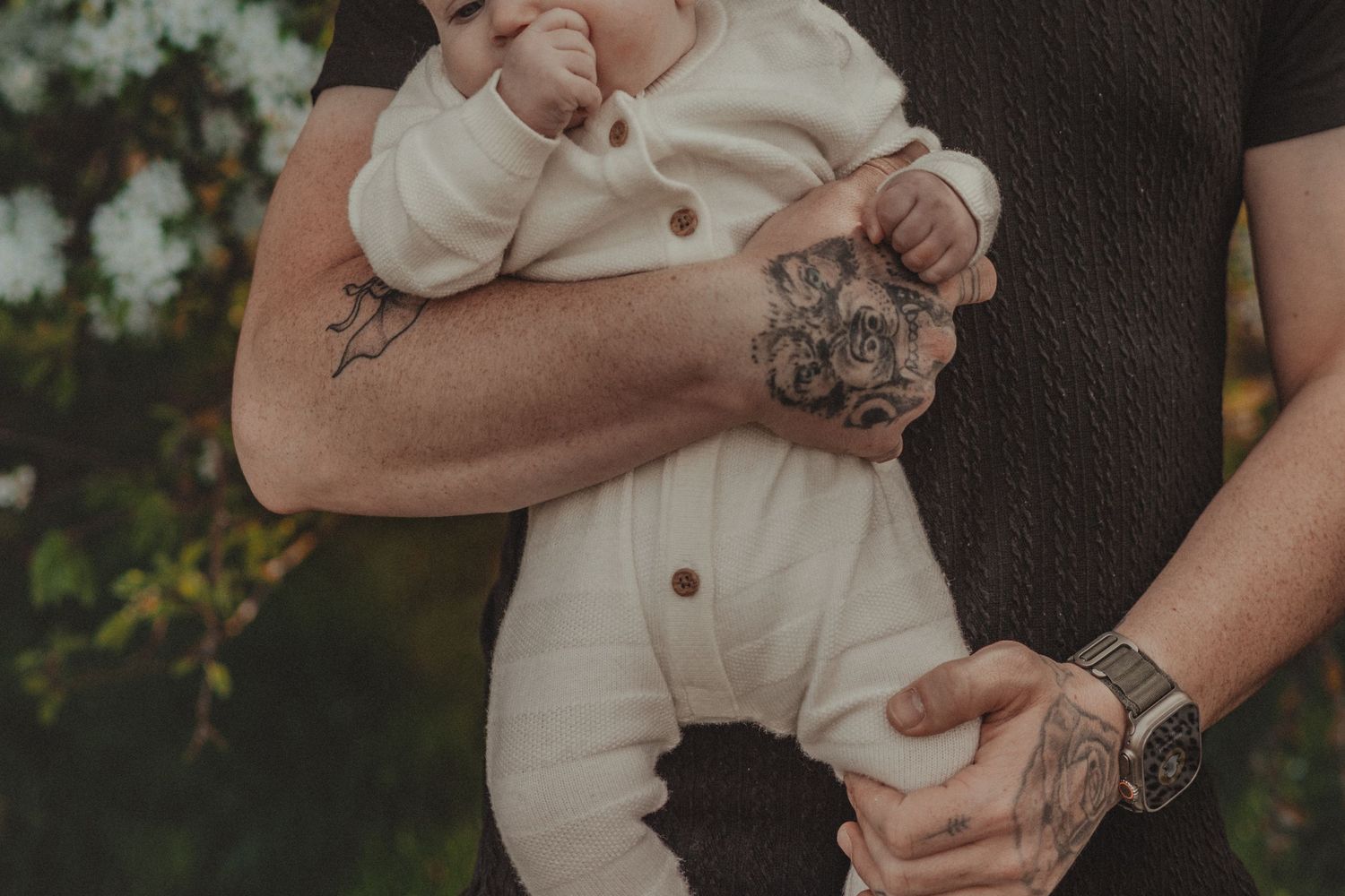 baby held in dads arms, tattooed hands, colour and grain at Needham Lake, Suffolk, in colour muted tones