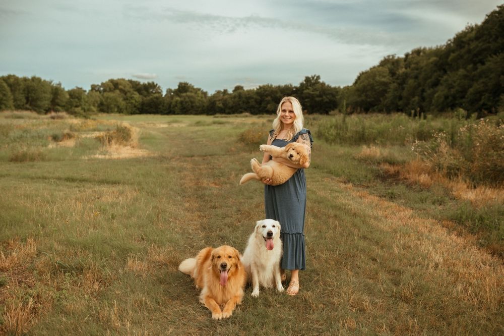Two friendly dogs sitting on a grassy hill path beside their companion on a cloudy day.