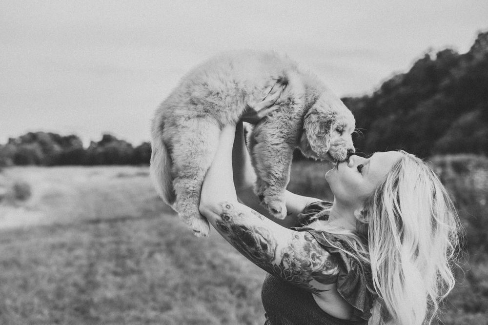 Playful moment with puppy being lifted up against cloudy sky in black and white photo.