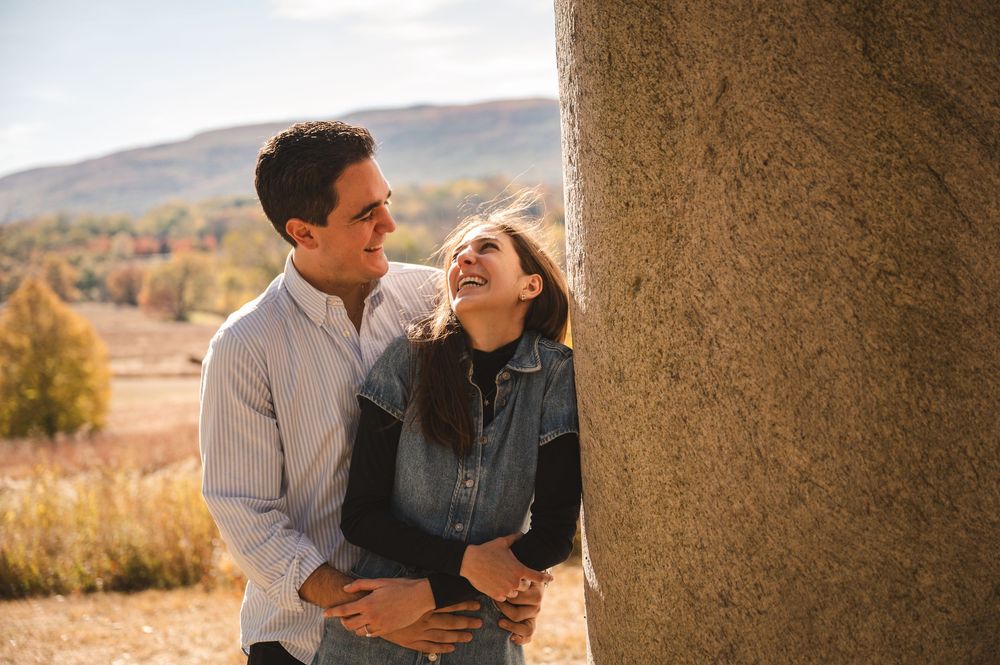 A couple embraces against a rocky backdrop in golden mountain scenery during a romantic proposal photo session.