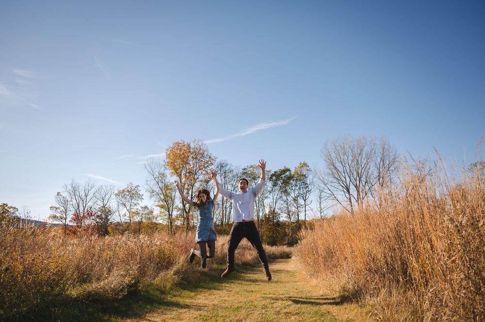 Two people enjoy a peaceful evening stroll through tall golden grass and autumn trees at sunset.