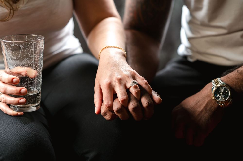 Close-up of hands together on a couch, with one person holding a glass and another wearing a watch.