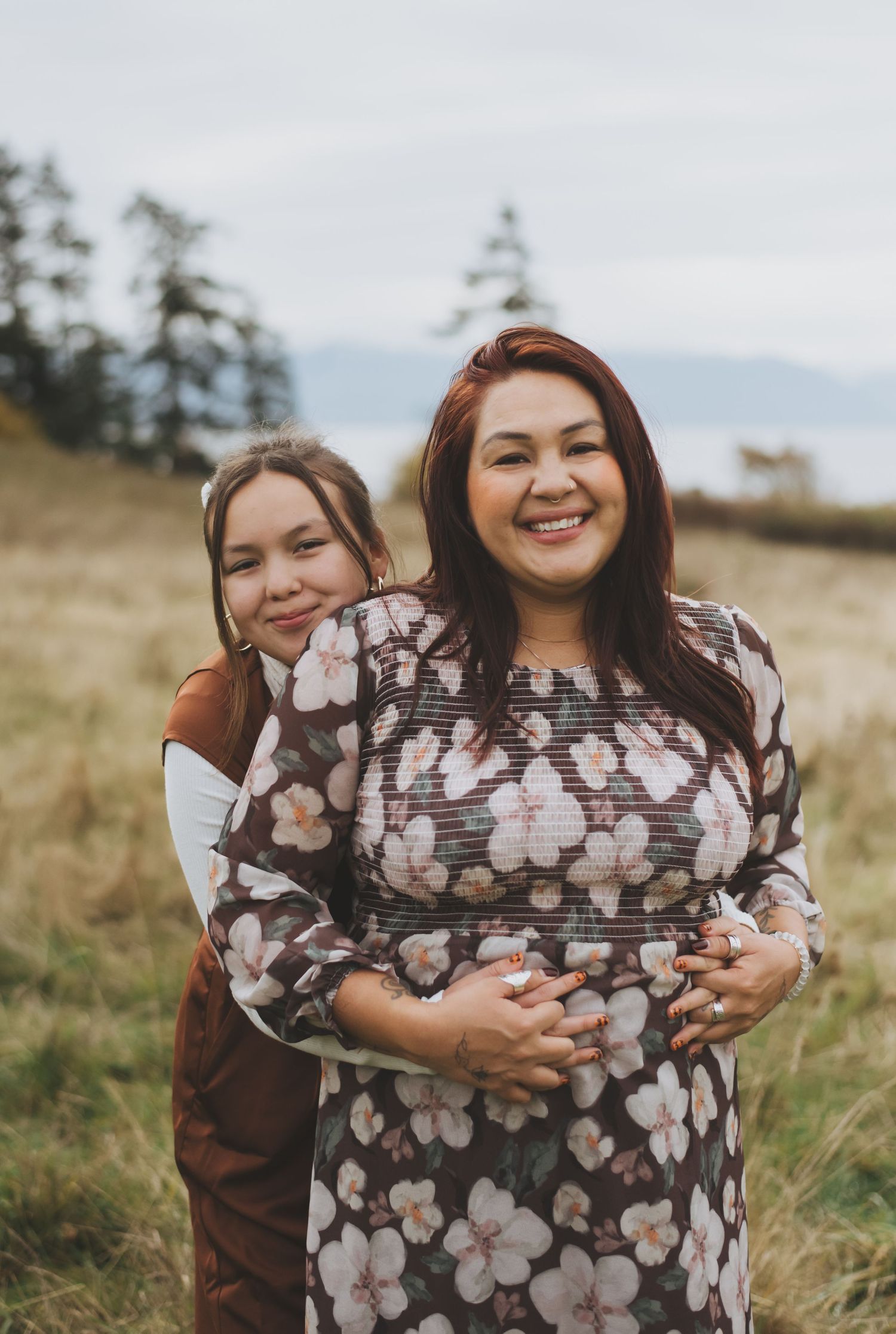Daughter hugging her mother from behind in an open field.