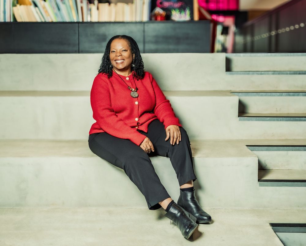 A person in a bright red sweater sits casually on concrete steps, smiling warmly at the camera.