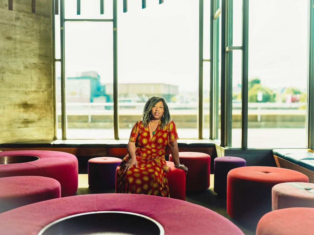 Person in a red polka dot dress sits among curved red seating in a modern space with large windows.