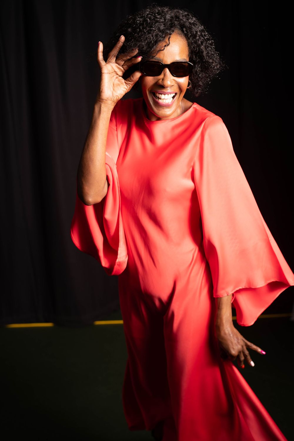 A woman in a flowing red dress dances joyfully against a dark background with expressive hand gestures and movement.