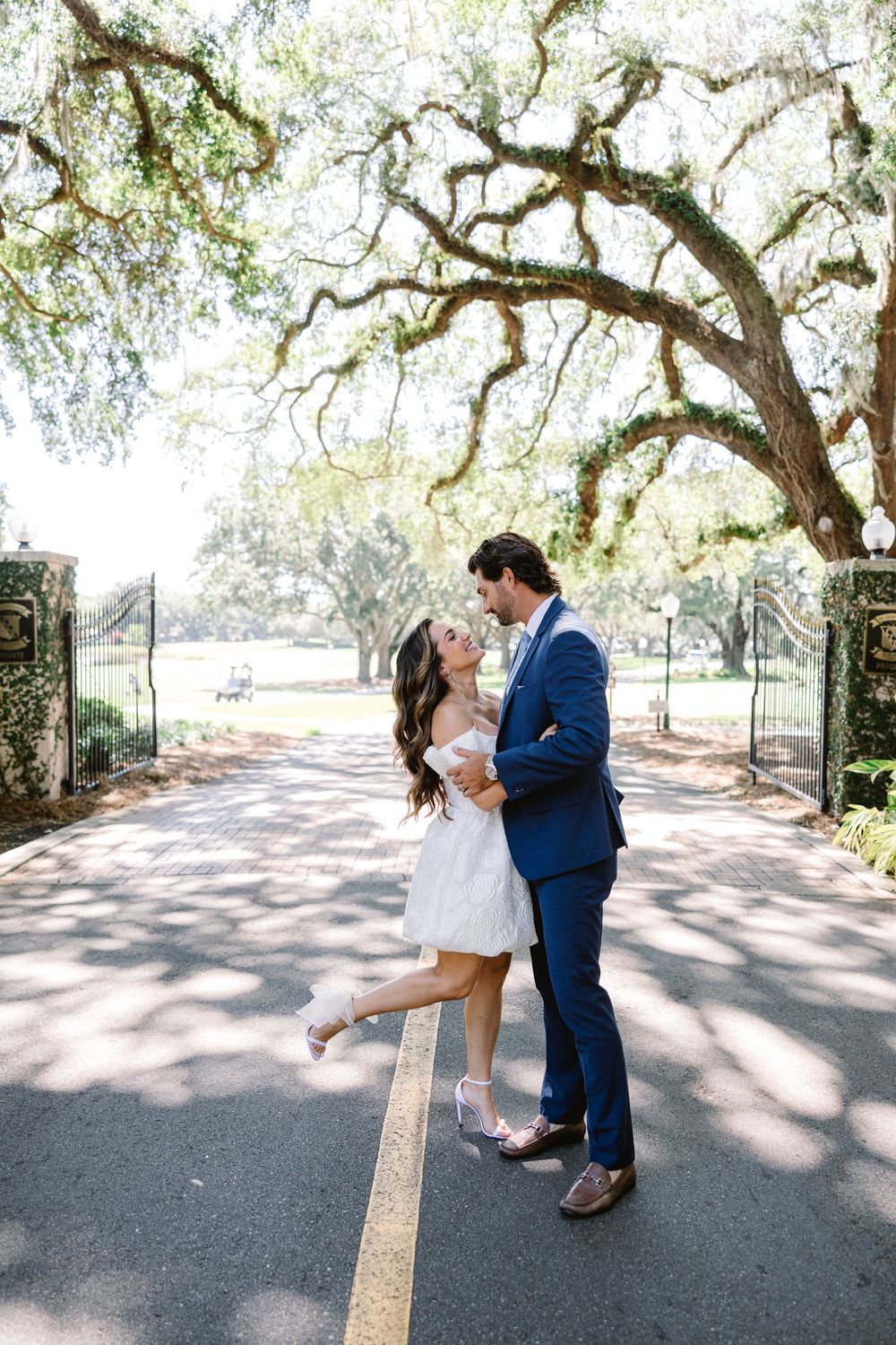 A couple sharing a romantic moment under mossy oak trees on a paved path.