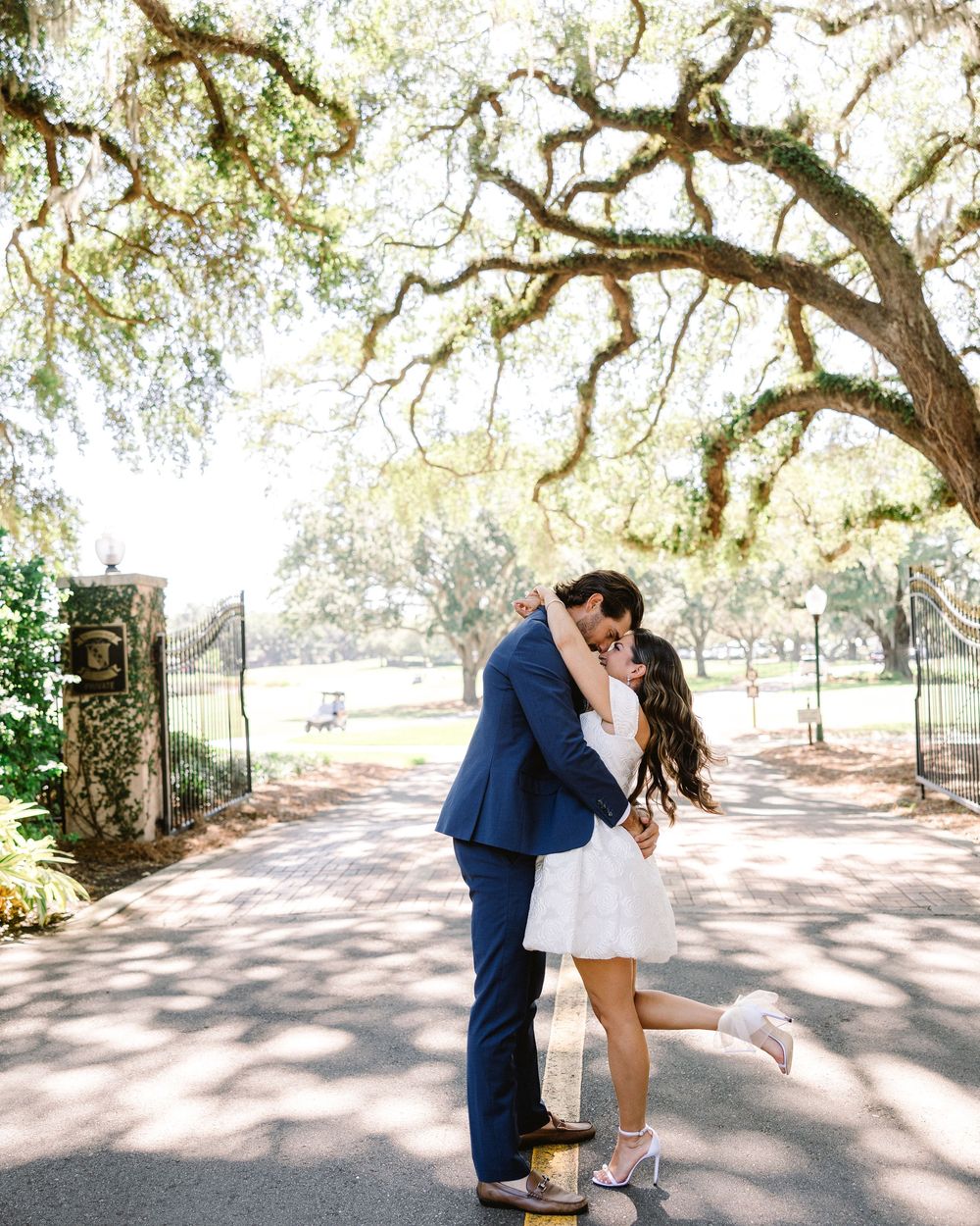 Couple embracing outdoors under a large oak tree with dappled sunlight.