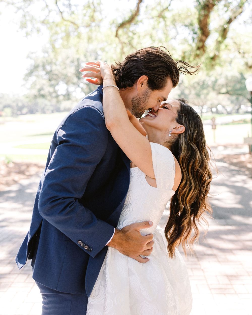 Joyful romantic embrace captured in a sun-dappled outdoor setting.
